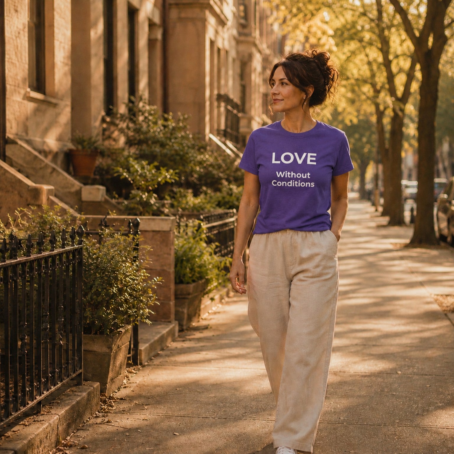 Woman wearing a purple 'LOVE Without Conditions' t-shirt walking down a sunlit street.
