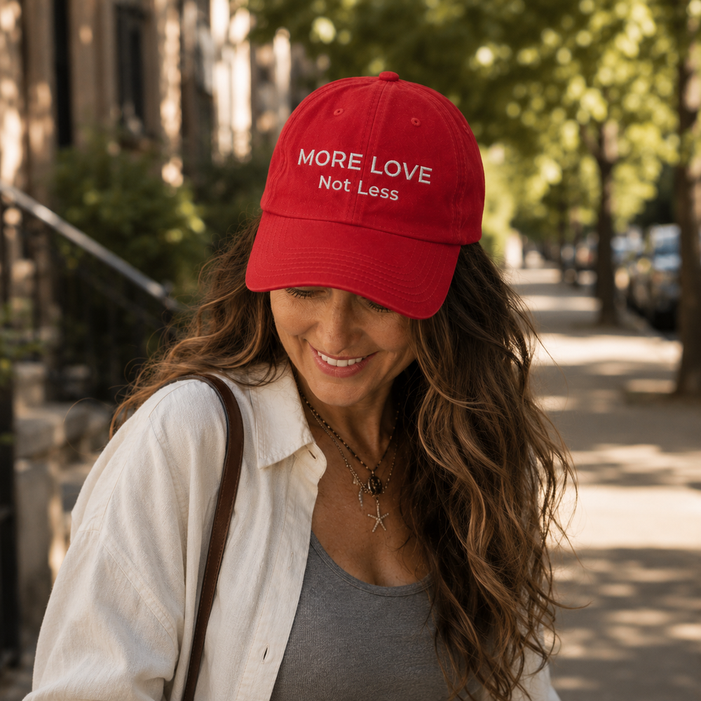Woman wearing a red cap with 'More Love Not Less' text on a sunny street.