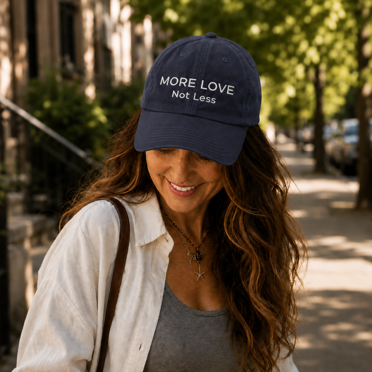 Woman wearing a navy blue cap with 'More Love Not Less' text, standing outdoors.