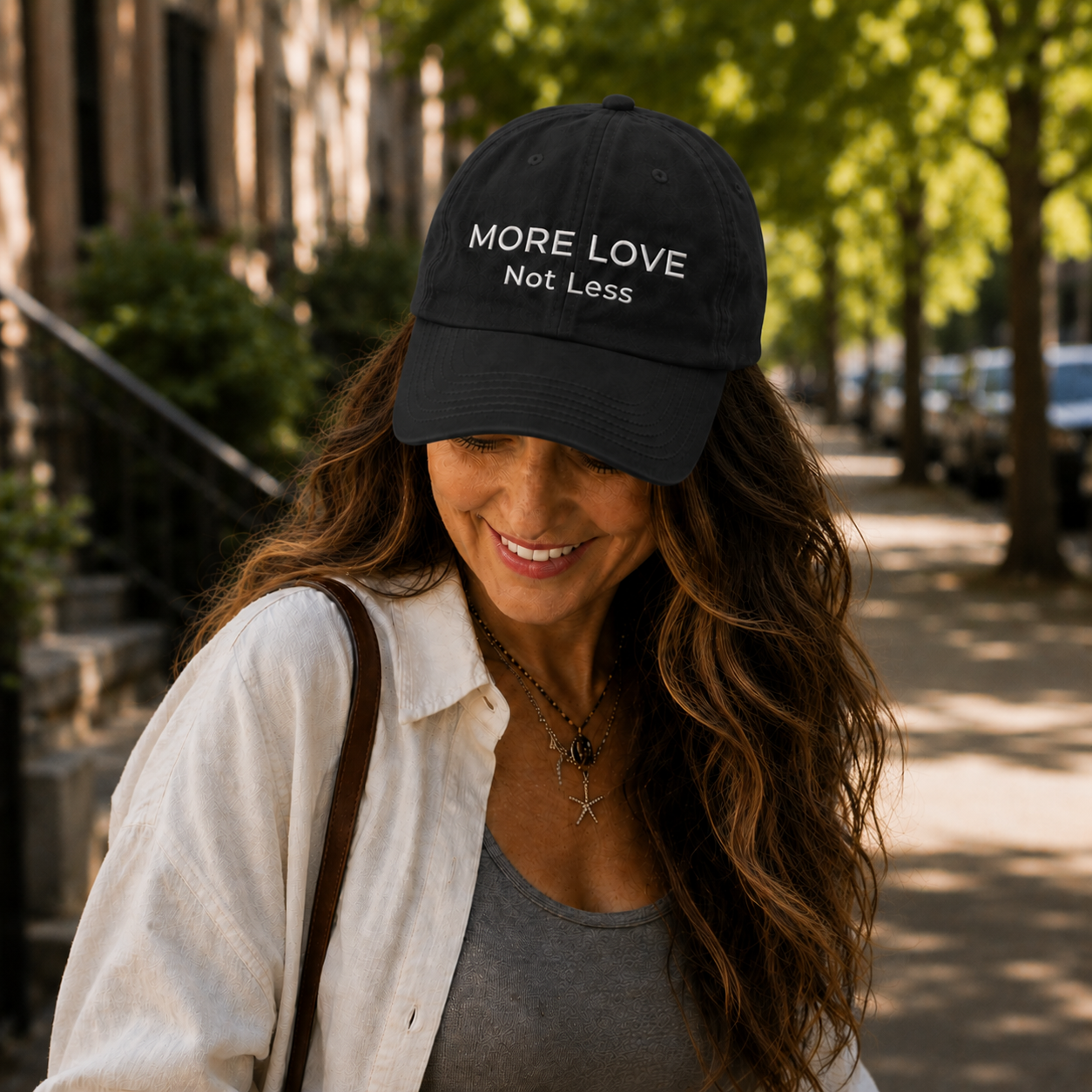 Woman wearing a black cap with 'More Love Not Less' text on a street.