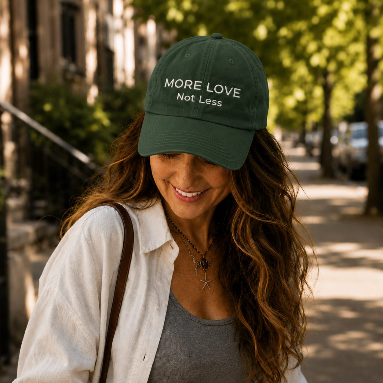 Woman wearing a dark green cap with 'More Love Not Less' text, standing outdoors.