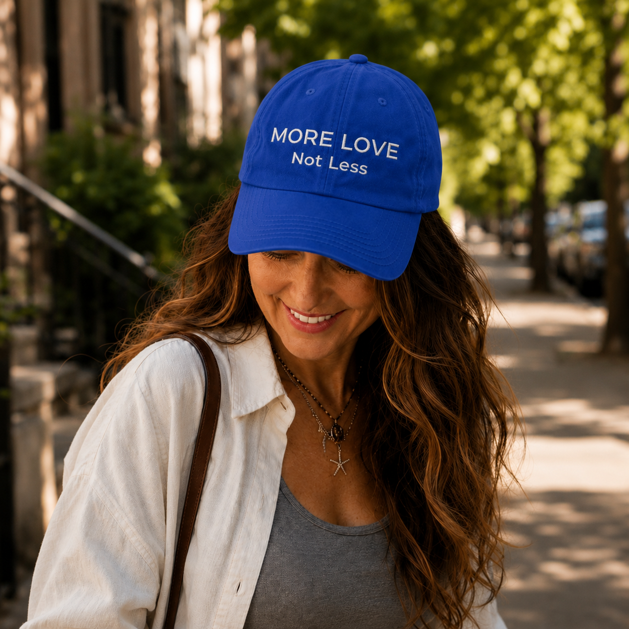 Woman wearing a blue cap with 'More Love Not Less' text on a sunny street.